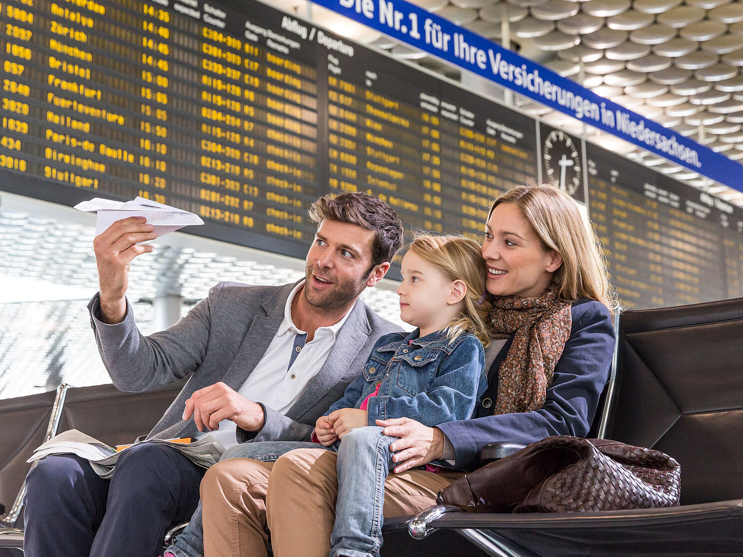 Familie mit Kind sitzt unterhalb der Fluganzeigetafel