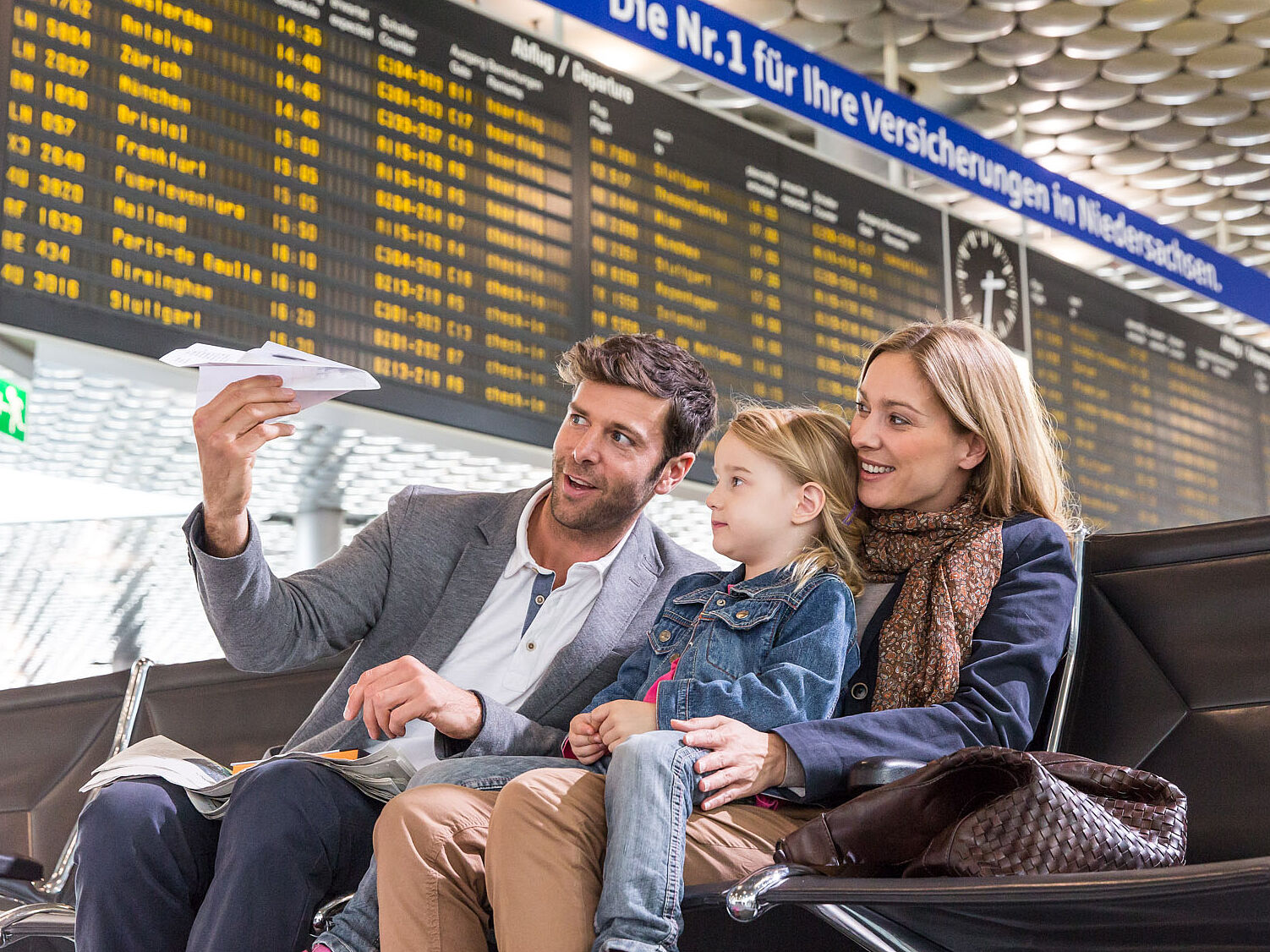 Familie mit Kind sitzt unterhalb der Fluganzeigetafel