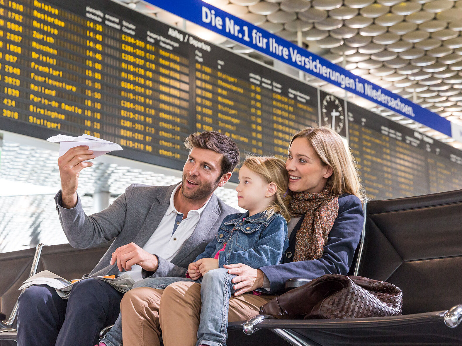 Familie mit Kind sitzt unterhalb der Fluganzeigetafel