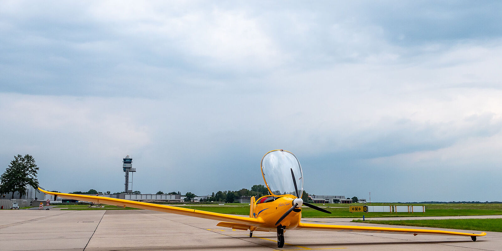 Das gelbe Motorsegelflugzeug steht auf dem Vorfeld vor GAT1