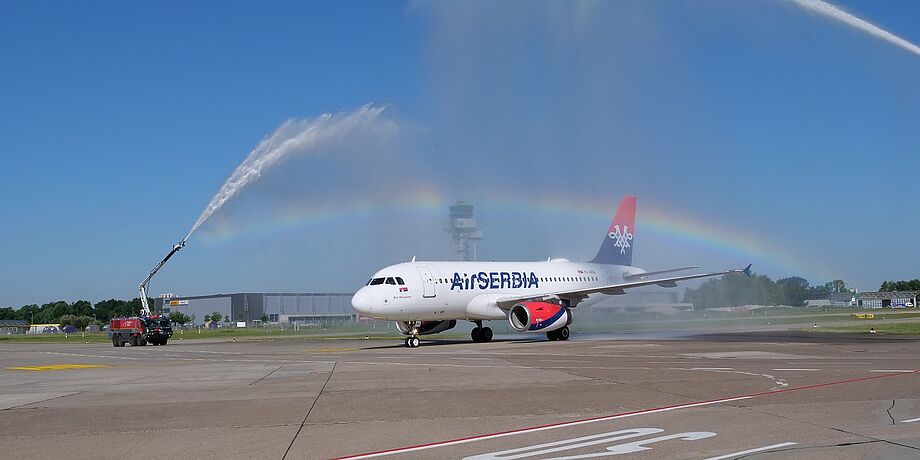 Das Flugzeug rollt durch einen Wasserbogen, der von zwei Fahrzeugen der Feuerwehr erzeugt wird.