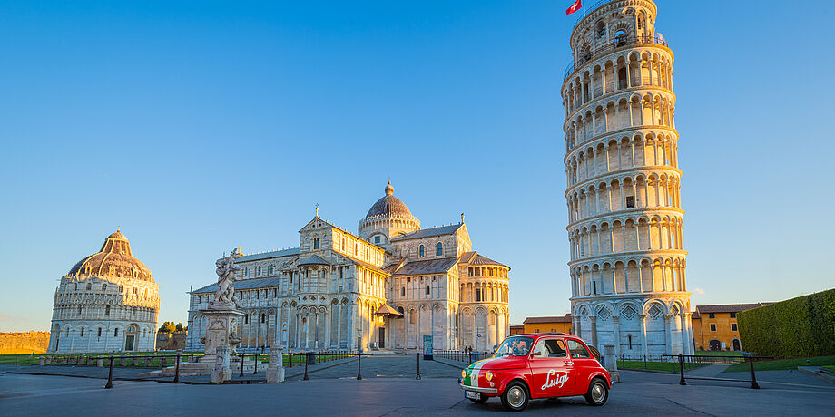 Ein kleines rotes Auto steht vor dem schiefen Turm von Pisa