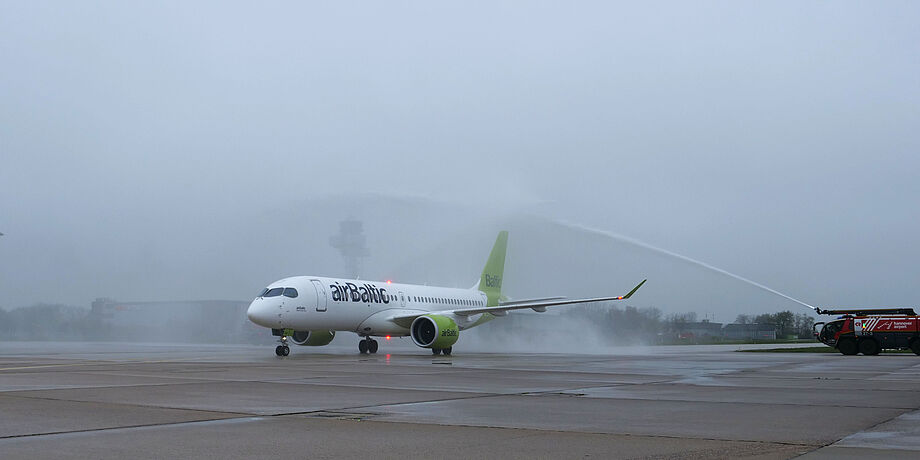 Das Flugzeug rollt durch einen Wasserbogen, der von zwei Fahrzeugen der Feuerwehr erzeugt wird.